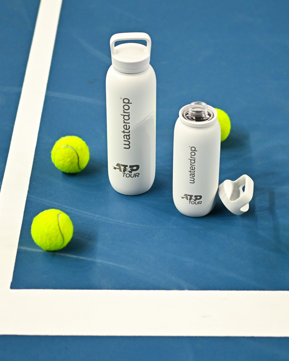 Two white Official ATP Tour waterdrop all-purpose Thermo Bottles with Spout Lids, alongside a tennis ball, on a blue surface.