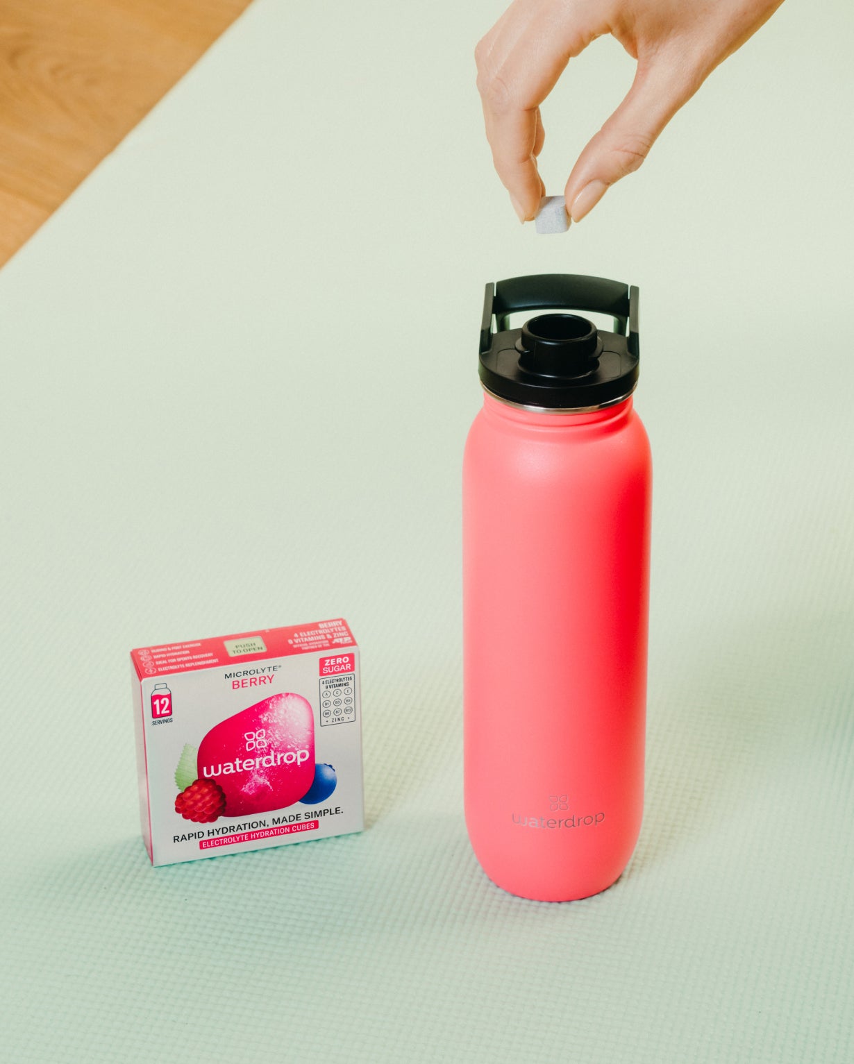 Hand placing a sugar cube into the All-Purpose Ultralight water bottle with Swing Lid, designed for easy hydration and hygiene.