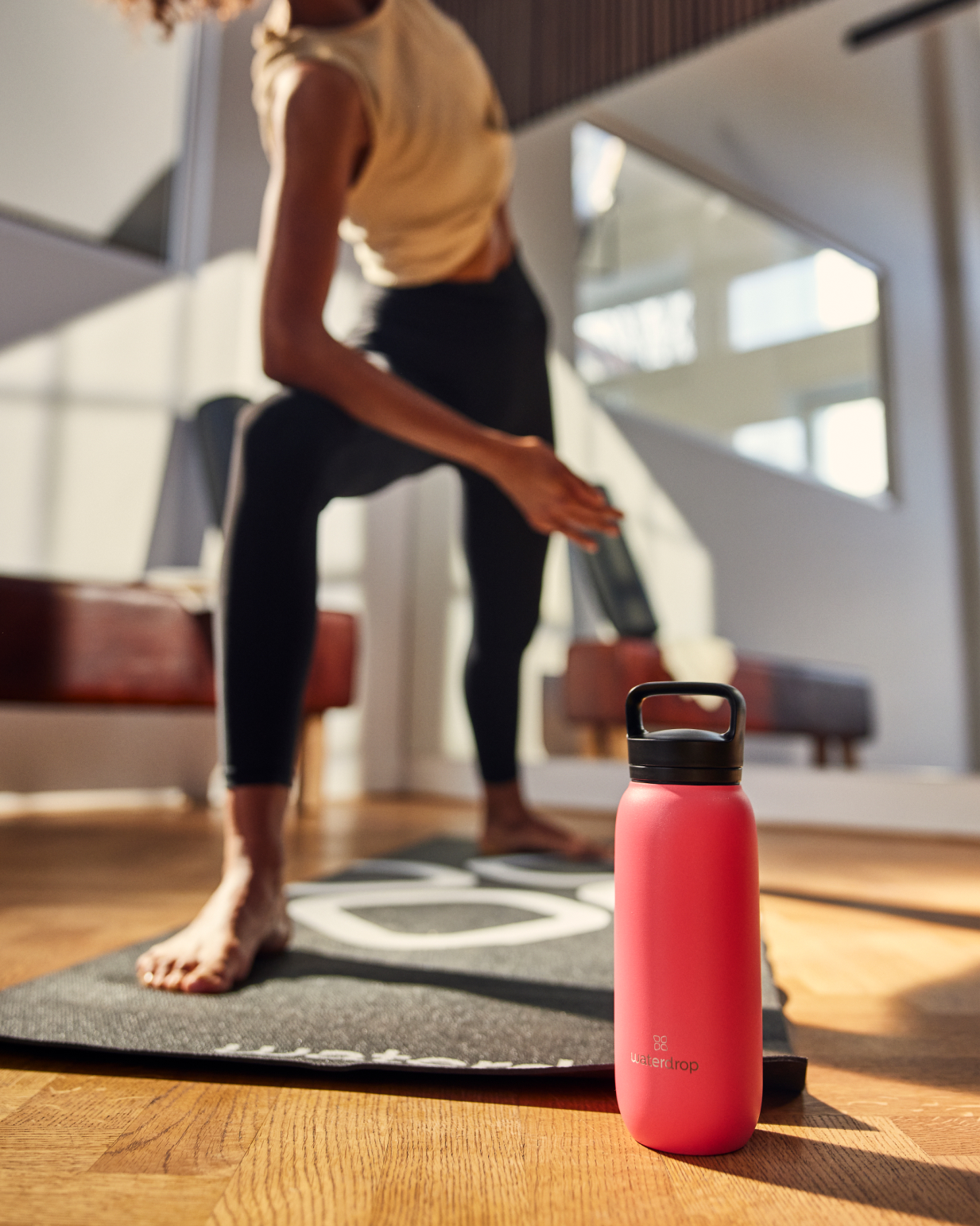 A woman standing on a mat, holding the All-Purpose Thermo Bottle with Spout Lid, ideal for keeping drinks ice-cold for up to 24 hours.