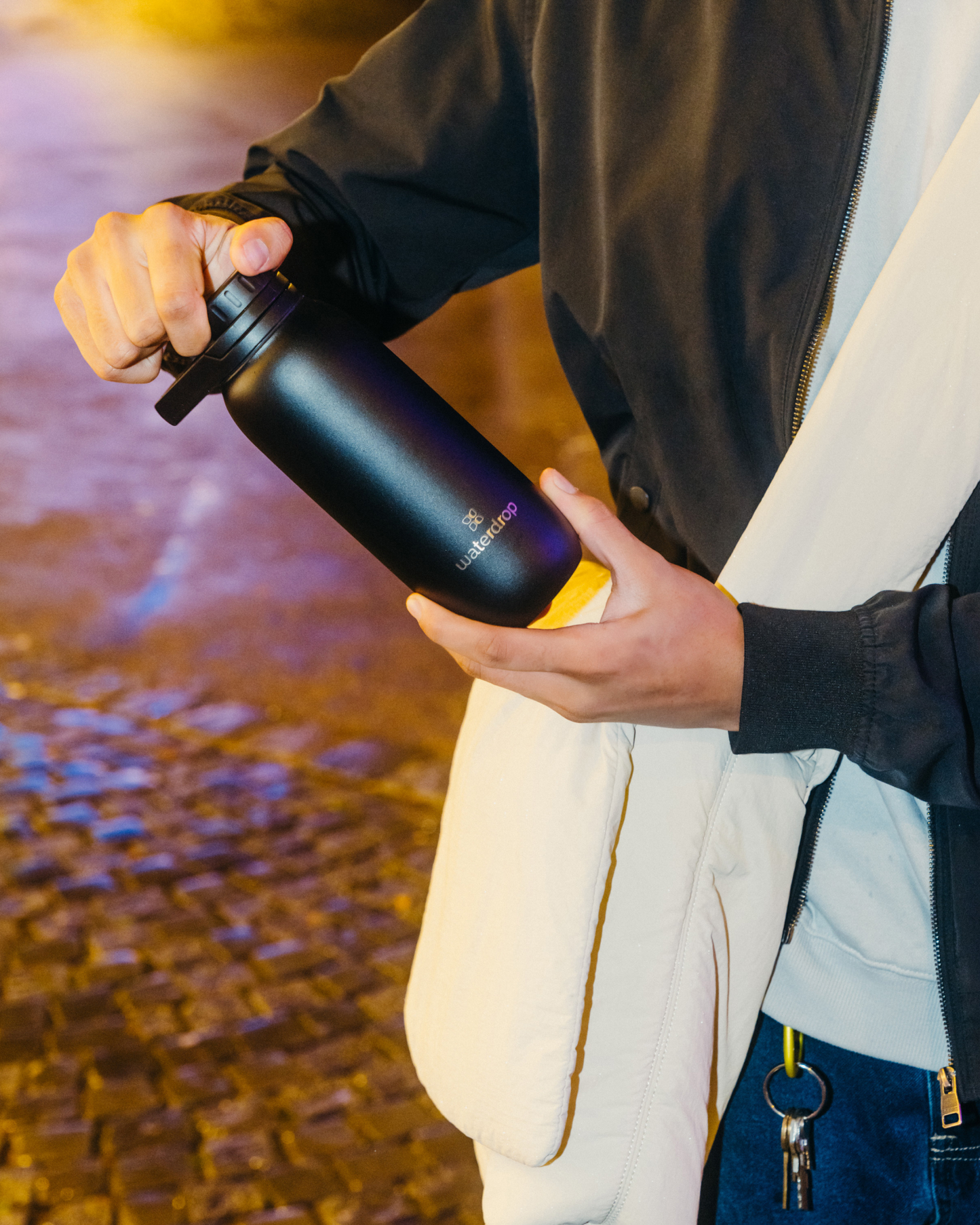 Person holding a black water bottle with an attached cap for hygienic, all-purpose use, featuring the Swing Lid design.
