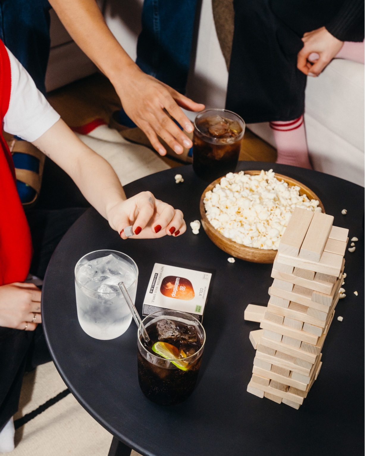 A table with a bowl of popcorn, a wooden block tower, and a cola drink in a glass with ice and a lime slice.