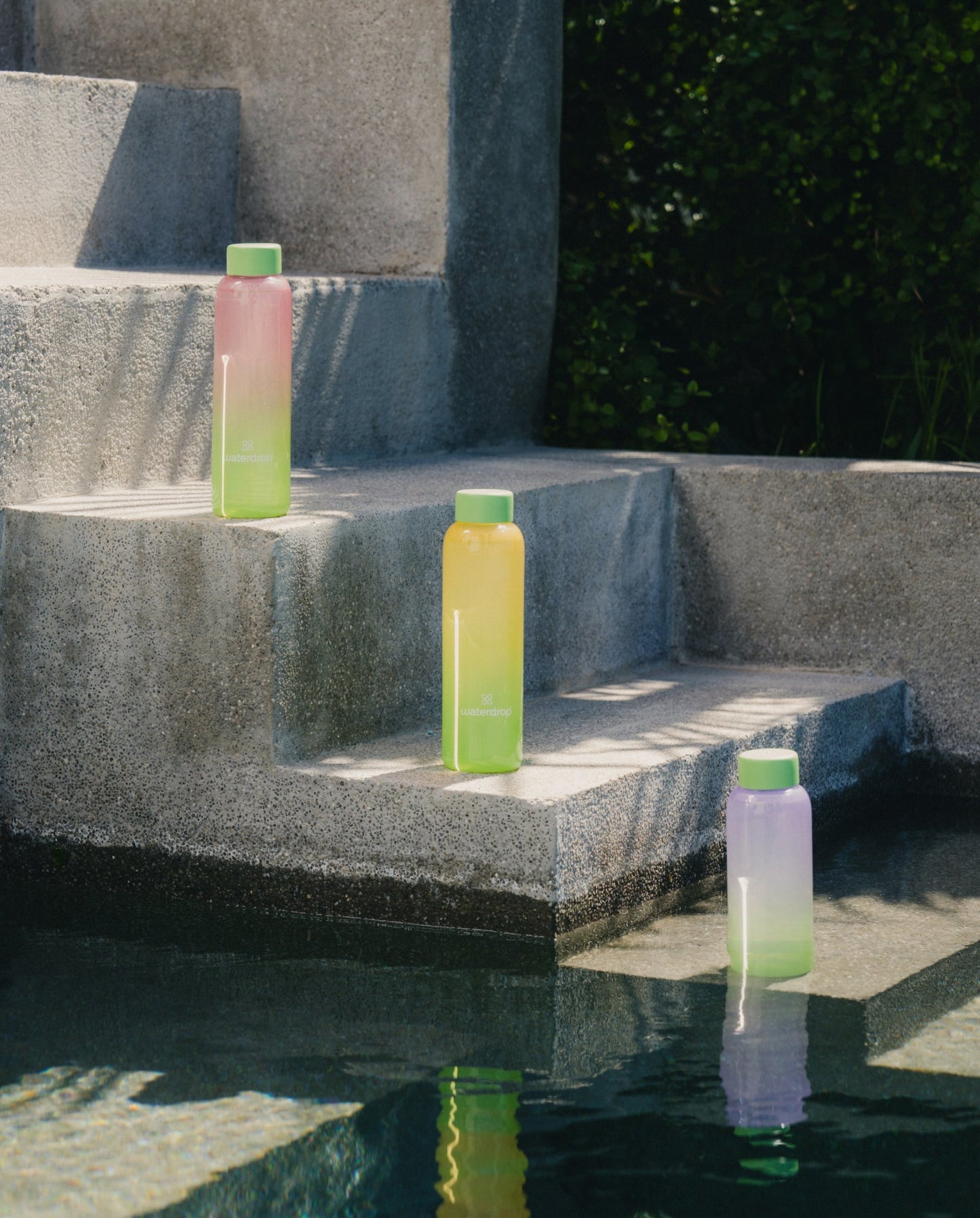 Summer Glass bottle on pool steps, showcasing its sophisticated borosilicate design. Ideal for pairing with refreshing Microdrinks, embodying year-round summer vibes.