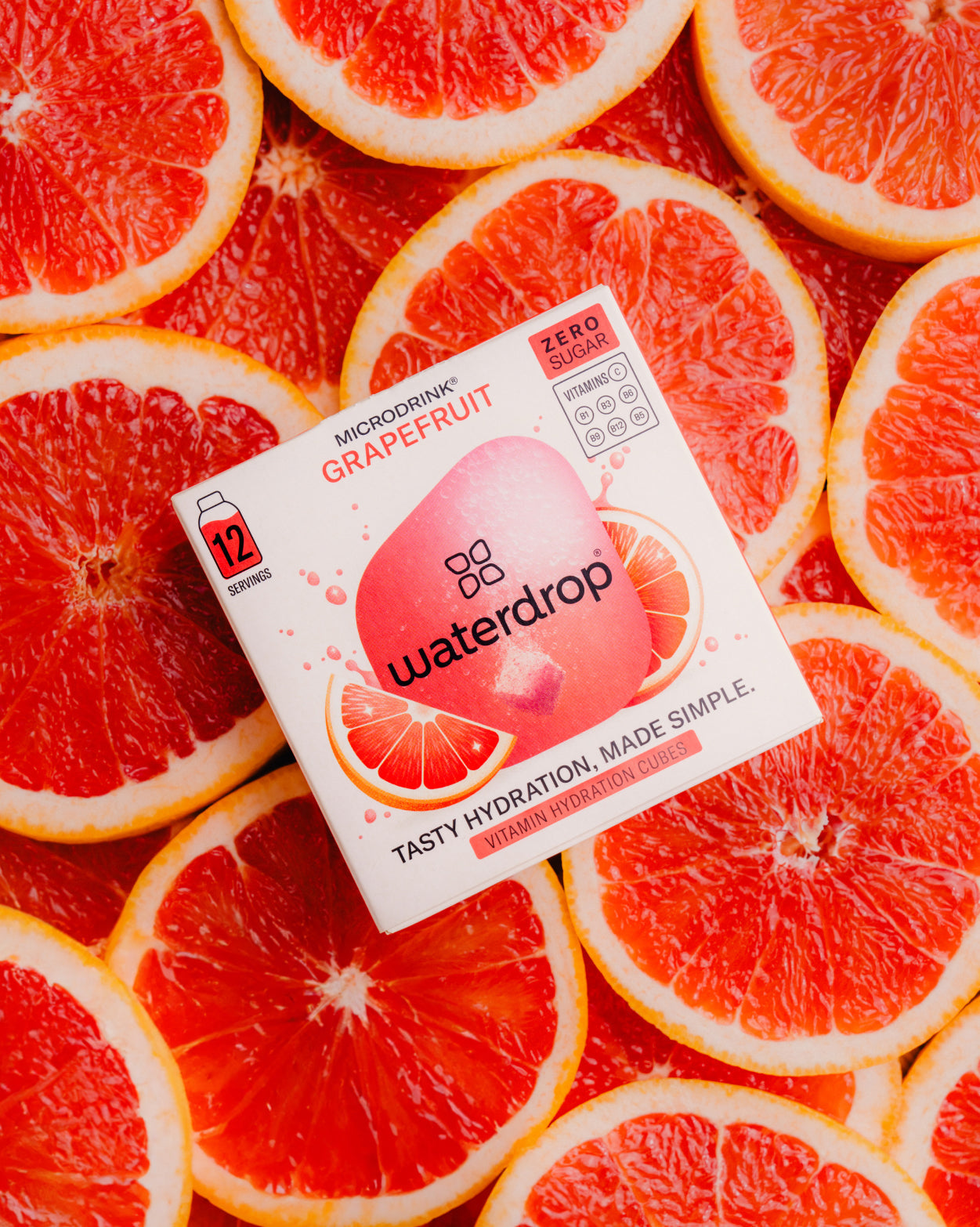 Box of waterdrop® GRAPEFRUIT juice on sliced grapefruits, offering a tangy, sugar-free burst of tart sweetness.