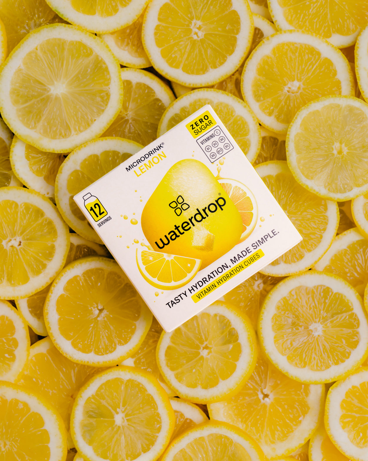 Box of LEMON drops on sliced lemons, highlighting citrus flavor with no sugar. Enjoy a tangy burst in every drop from waterdrop® EU.