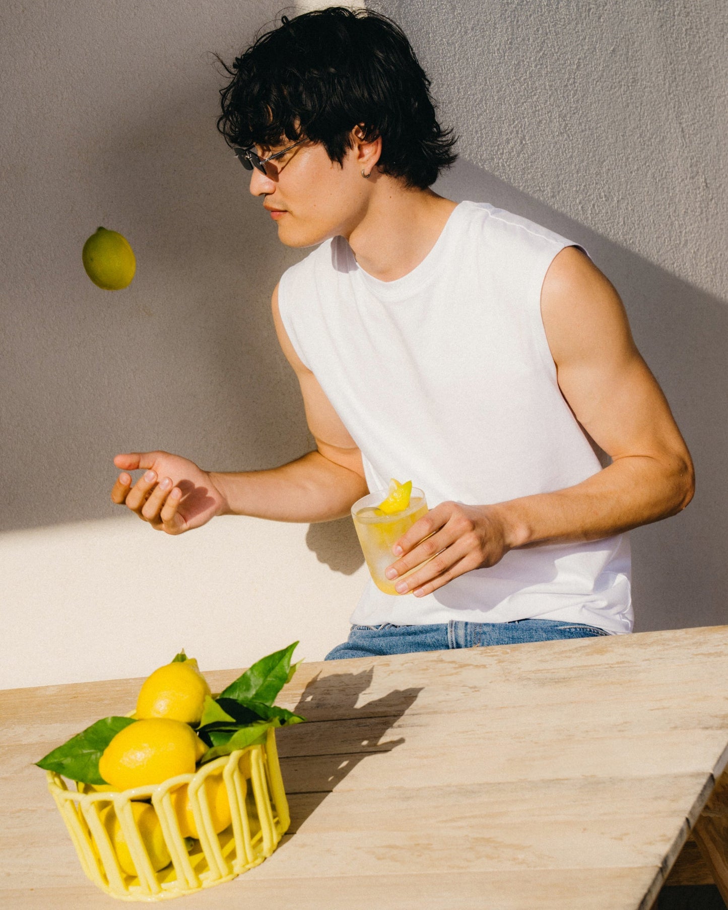 A man in a white shirt drops a lemon into a glass, with a basket of lemons nearby, representing the citrusy burst of LEMON.