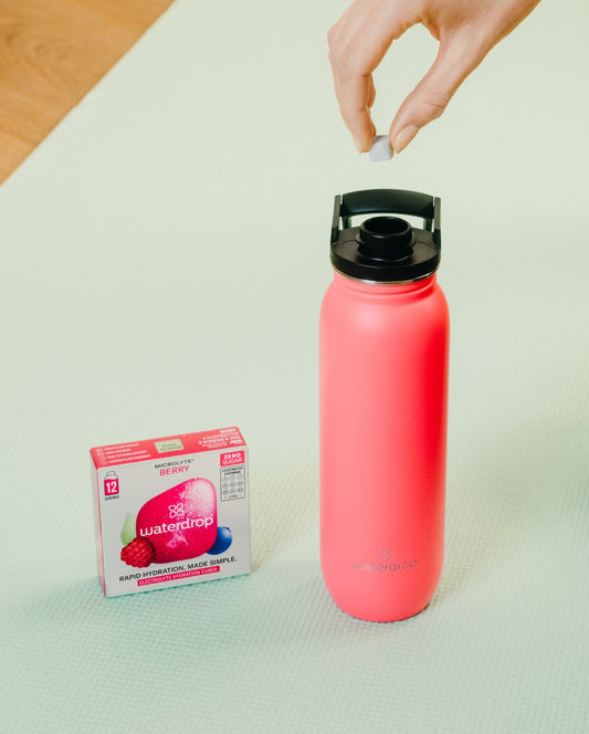 Hand placing a sugar cube into the All-Purpose Ultralight water bottle with Swing Lid, designed for easy hydration and hygiene.