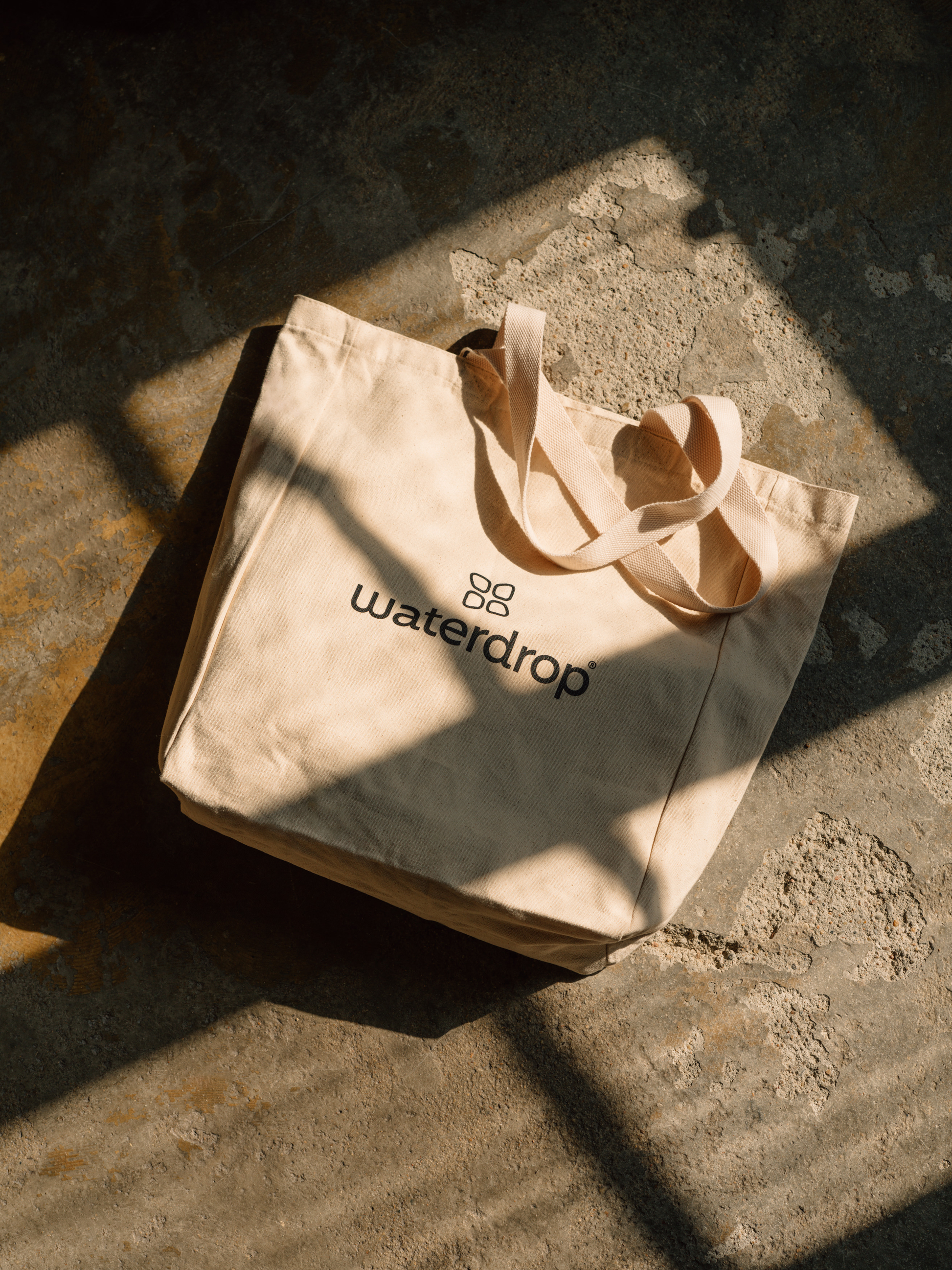 Shopping Bag on concrete surface, made of high-quality cotton, spacious enough for shopping and a water bottle with waterdrop® flavor.
