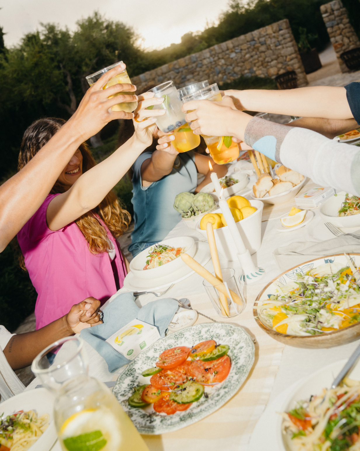 People clinking clear borosilicate glasses at a table with various dishes, celebrating with waterdrop® hydration products.