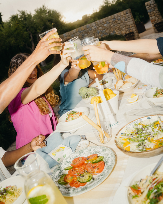People clinking clear borosilicate glasses at a table with various dishes, celebrating with waterdrop® hydration products.