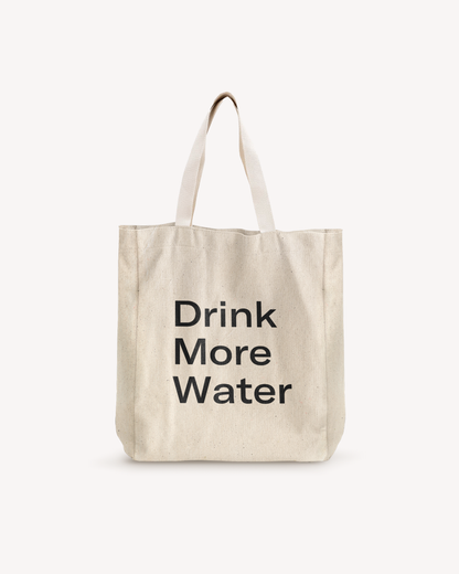 White cotton shopping bag with black text, featuring a sturdy white strap with a metal ring. Ideal for carrying a water bottle and essentials.