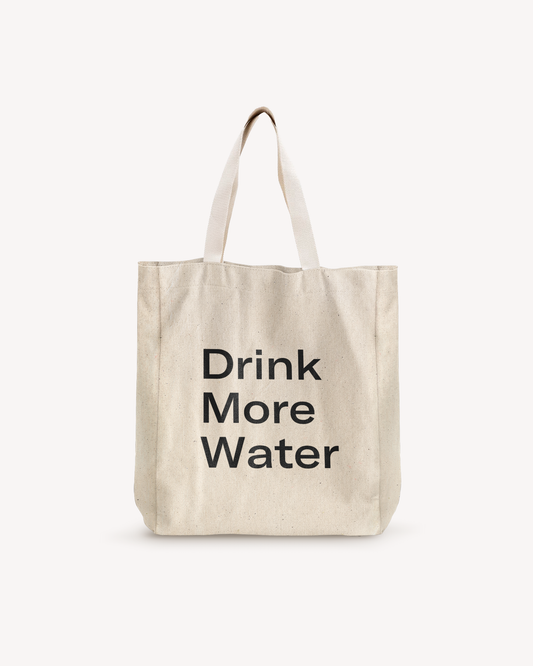 White cotton shopping bag with black text, featuring a sturdy white strap with a metal ring. Ideal for carrying a water bottle and essentials.