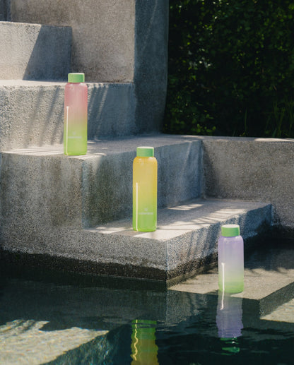 Summer Glass bottle on pool steps, showcasing its sophisticated borosilicate design. Ideal for pairing with refreshing Microdrinks, embodying year-round summer vibes.