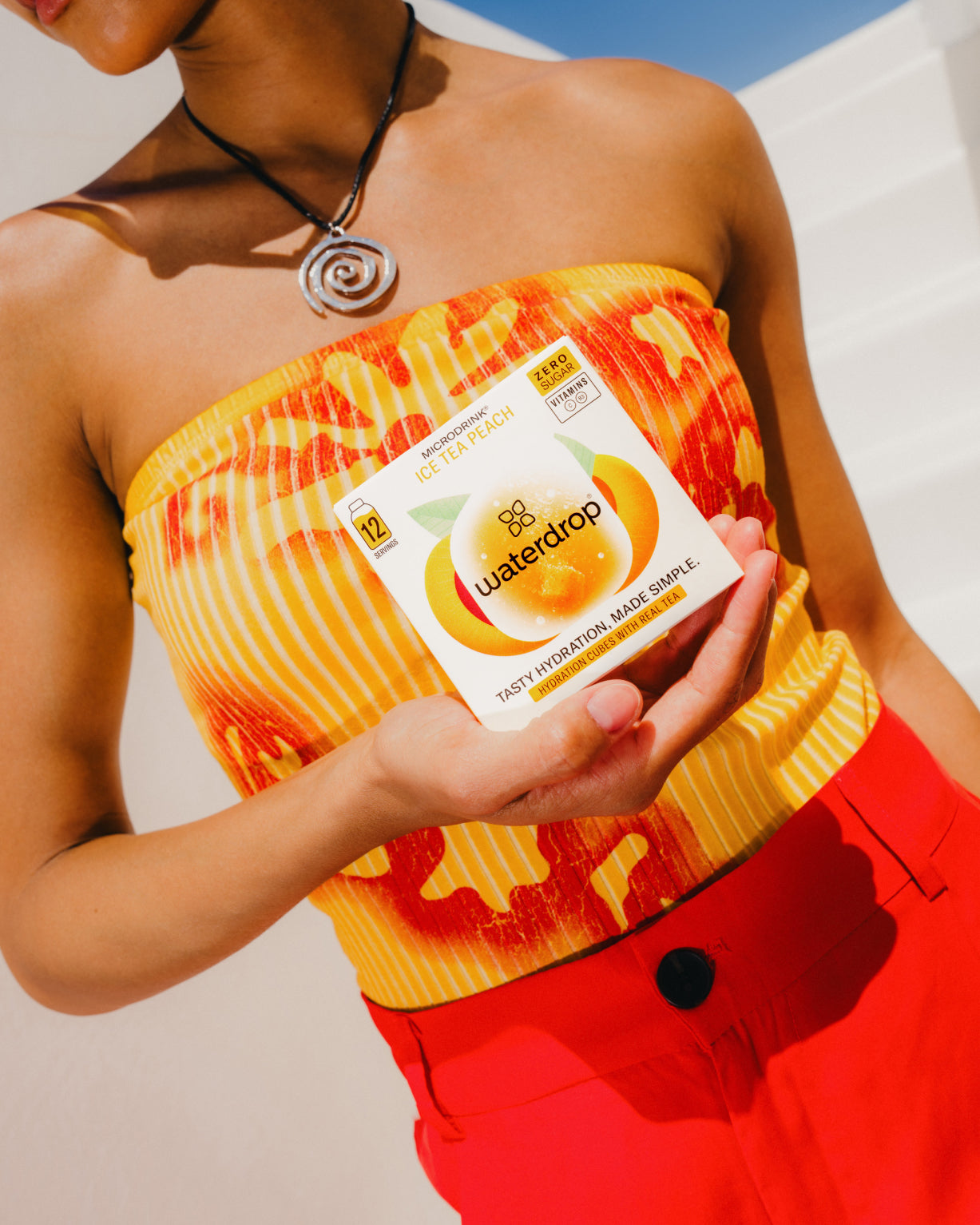 Person holding a box labeled ICE TEA PEACH by waterdrop®, showcasing a sugar-free, peach-flavored tea infusion.