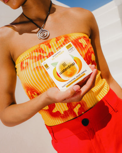 Person holding a box labeled ICE TEA PEACH by waterdrop®, showcasing a sugar-free, peach-flavored tea infusion.