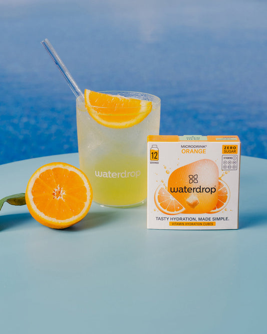 Glass of ORANGE juice with a straw, next to a box of ORANGE juice, and a half orange. Enjoy citrus flavor without the sugar.